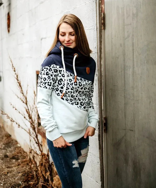 Woman wearing a hoodie with leopard print pattern standing against a white wall.